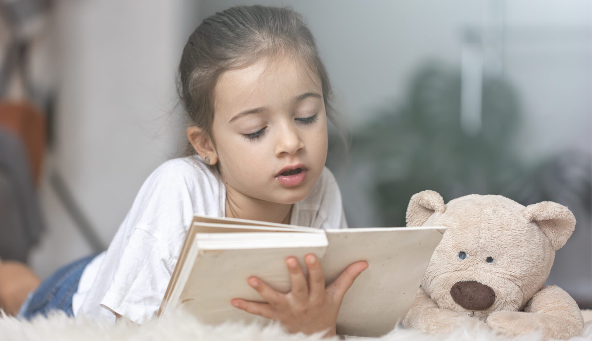 Little girl reads a book with a teddy bear