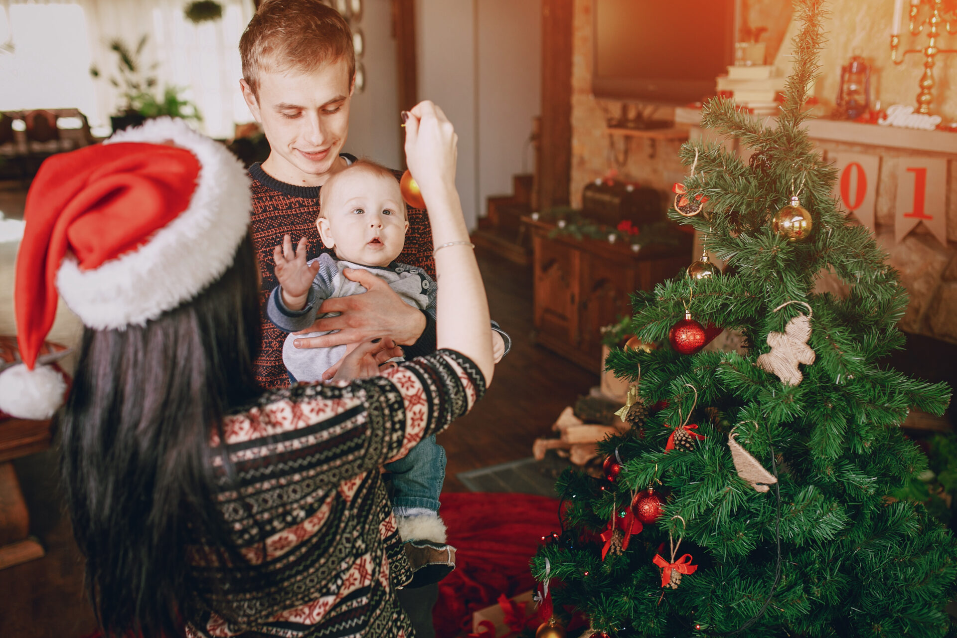 mother-distracting-baby-with-christmas-ornament-while-father-holds-it-his-arms